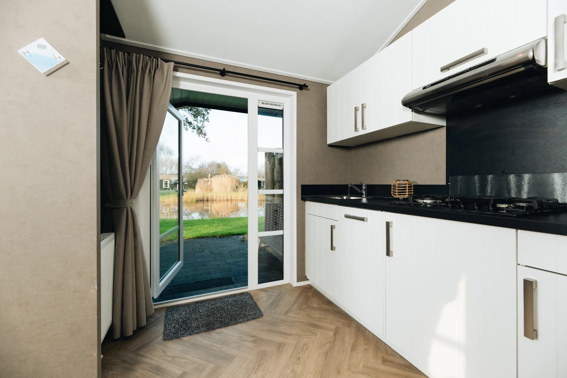 Witte moderne keuken in een vakantieverblijf met een zwart werkblad en een openstaande deur naar het privéterras met uitzicht op de vijver.